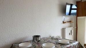 Un coin repas avec une table dressée pour quatre personnes, un téléviseur fixé au mur et un réfrigérateur en arrière-plan.