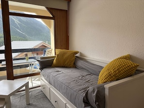 A room with a bed, a small table, and a window with a view of mountains.