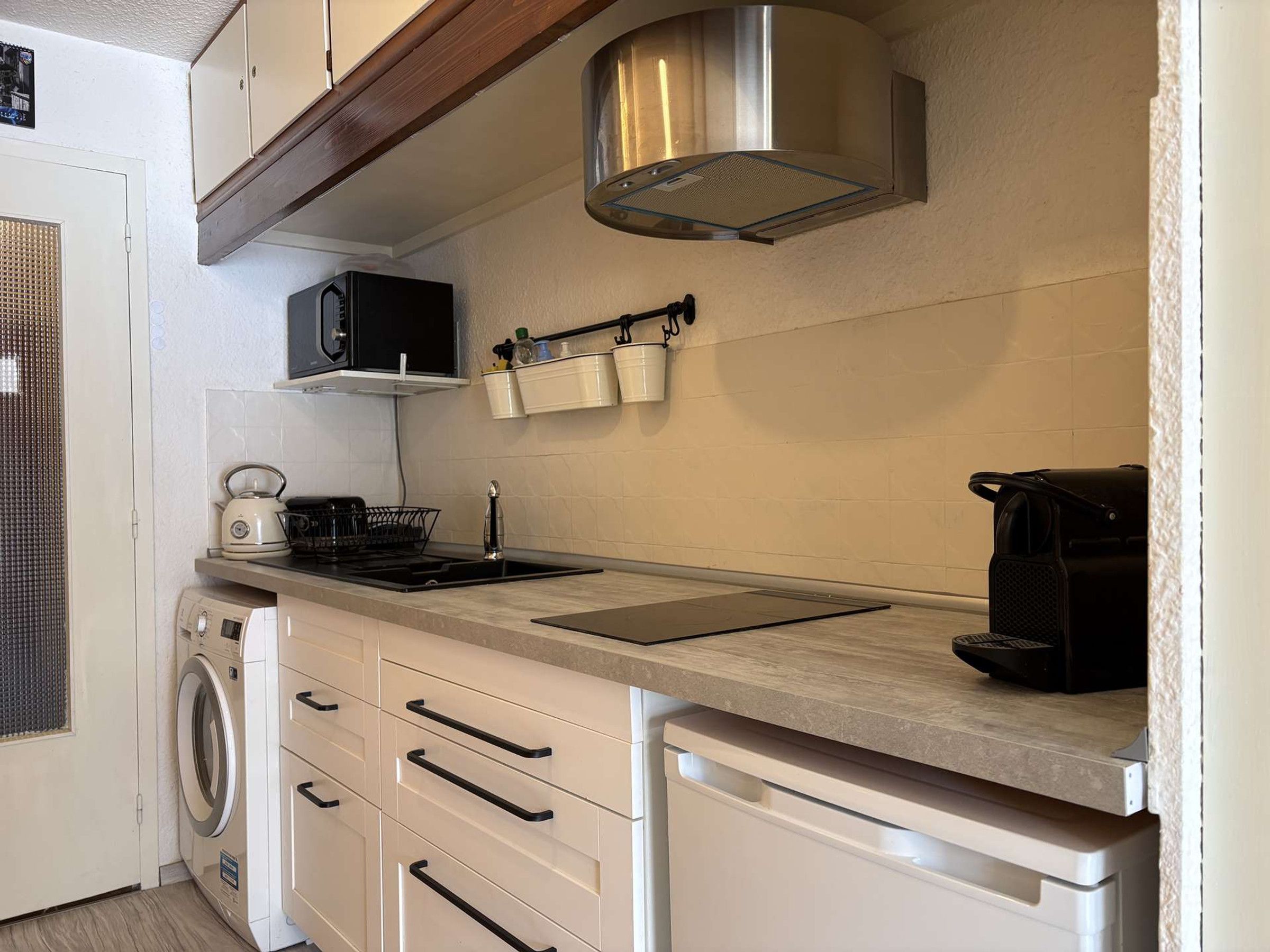 Cocina compacta con microondas, hervidor de agua y cafetera sobre la encimera, lavadora y lavavajillas.