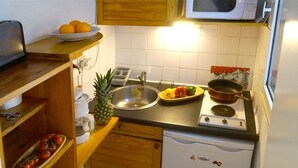 A compact kitchen with a sink, stove, and microwave. There are wooden cabinets and a small refrigerator. - Peaceful South-Facing Studio in Luchon with Balcony, Parking, and Mountain View (Bagnères-de-Luchon)