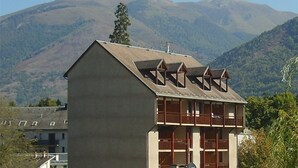 A building with a sloped roof and multiple dormer windows, set against a mountainous backdrop. - Peaceful South-Facing Studio in Luchon with Balcony, Parking, and Mountain View (Bagnères-de-Luchon)