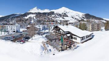Un hotel con techo nevado, estacionamiento y montañas al fondo.