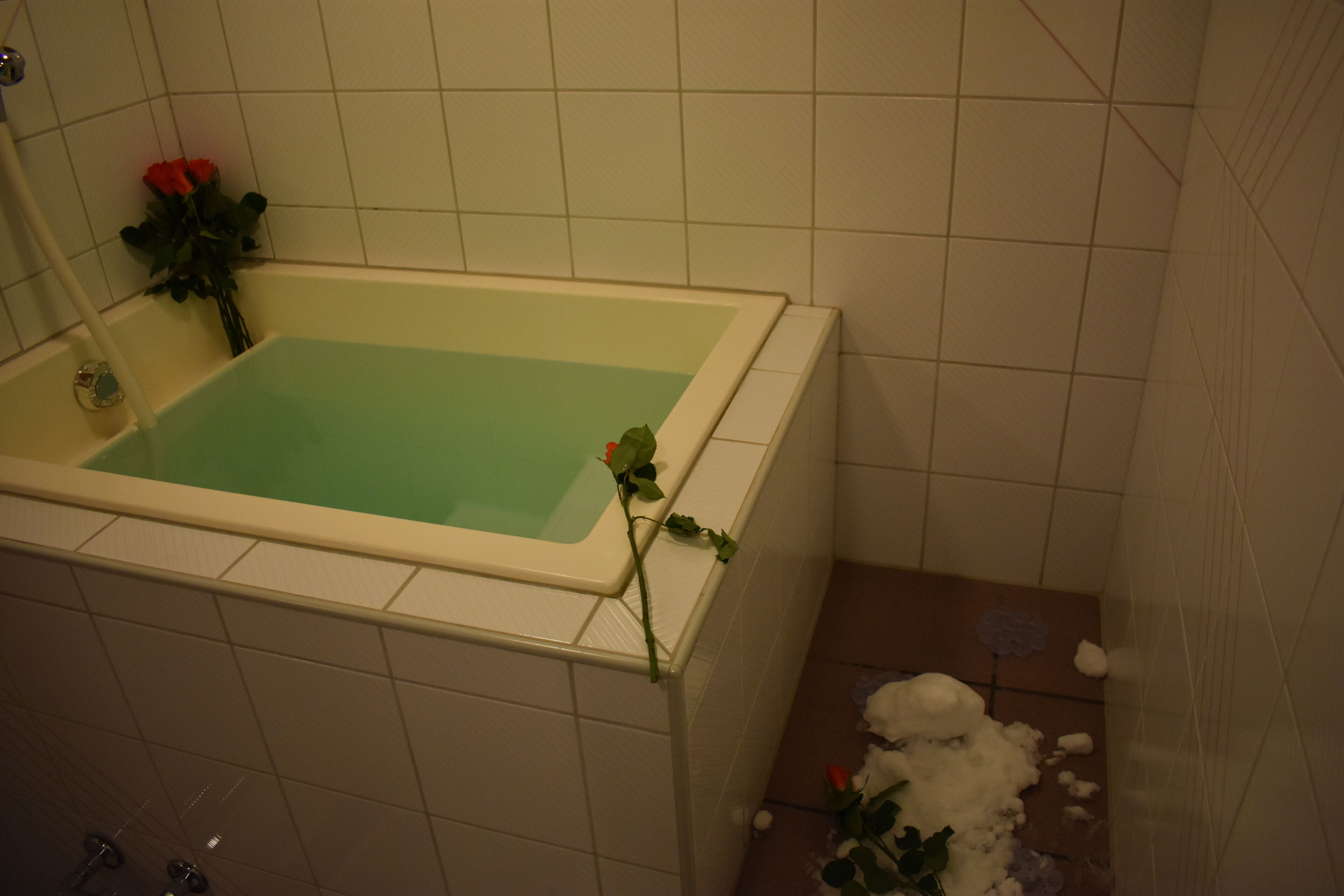 A bathtub with a greenish water color, a rose, and a shower area with white tiles.