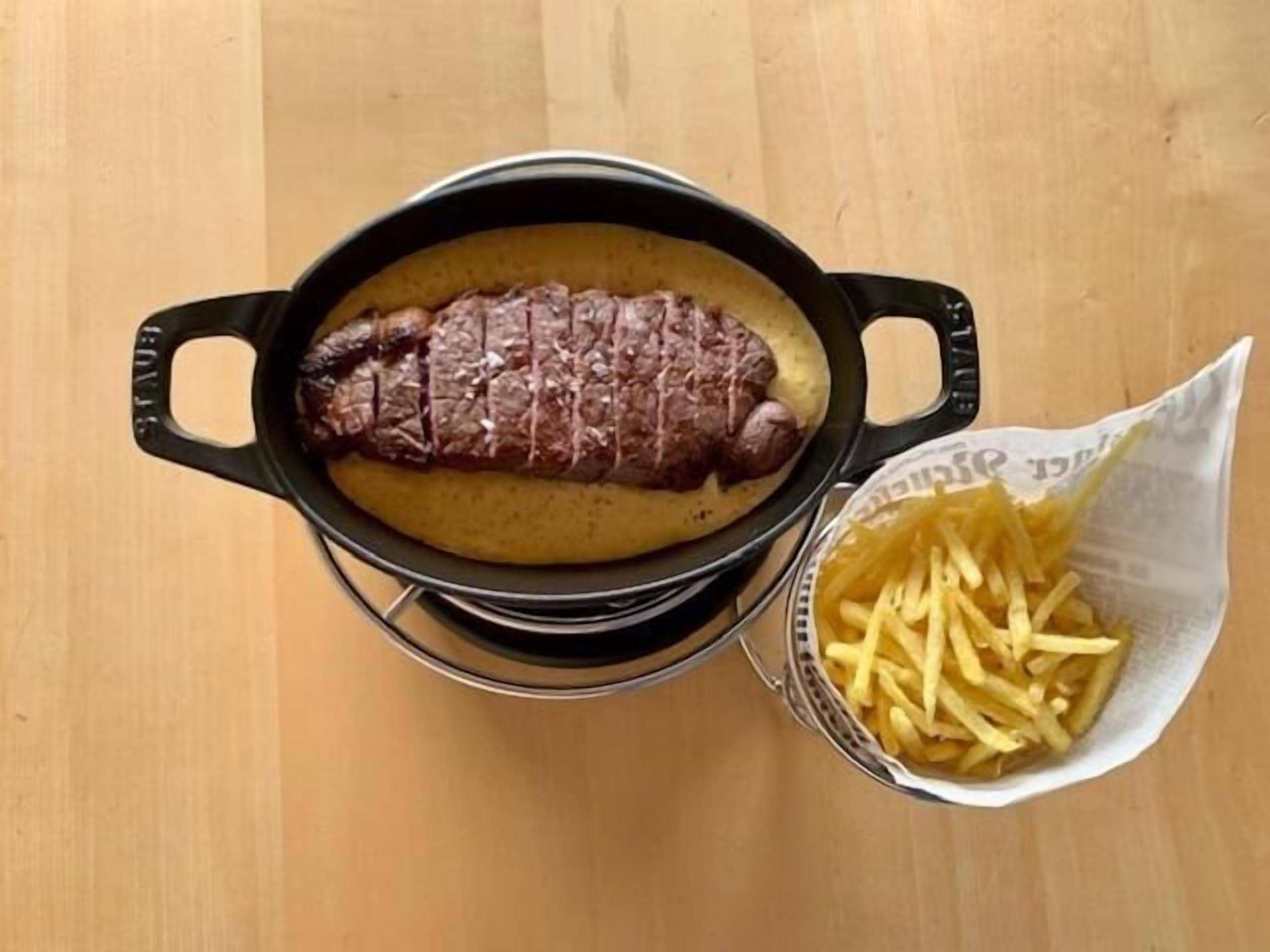 Un bistec en una sartén de hierro fundido sobre una mesa de madera.