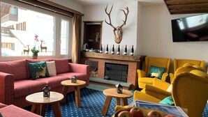 A cozy living room with a fireplace, a mounted deer skull, and a bowl of apples. - Hotel Bünda Davos (Davos)
