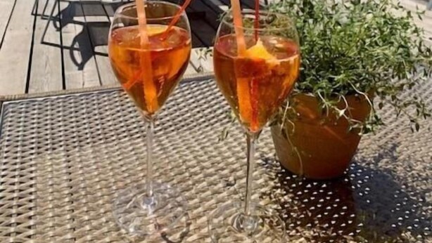 A table with two glasses of a beverage, outdoor seating with umbrellas, and a mountain view in the background. - Hotel Bünda Davos (Davos)