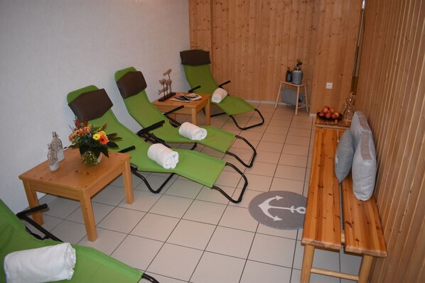 Une pièce comprenant quatre fauteuils de massage verts, une table en bois ornée d’un vase de fleurs et un banc en bois avec des serviettes.