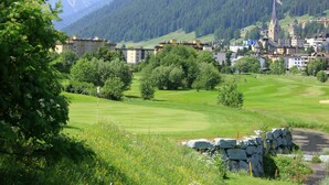 A golf course with a stone wall and a church in the background. - Hotel Bünda Davos (Davos)