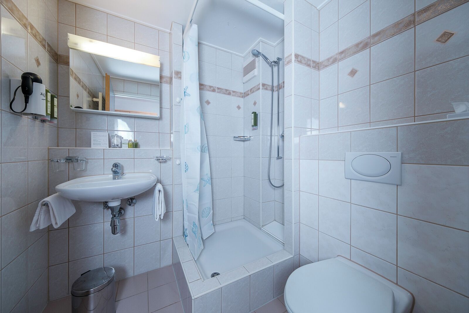 Een moderne badkamer met een wastafel, spiegel, douche en toilet.