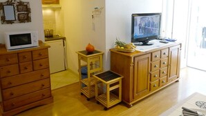 A compact living space with a kitchenette, wooden furniture, a television, and a clock on the wall.