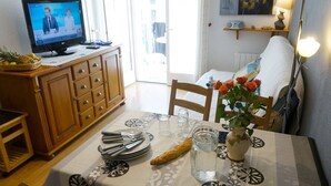 A dining area with a table set for two, a television on a cabinet, and a flower vase on the table.