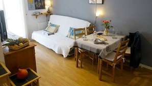 A cozy room with a bed, a dining table set for two, a small wooden side table, and a television.