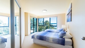 Un dormitorio con una cama grande, una mesita de noche y vistas al exterior a través de amplias ventanas.
