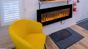 Une pièce avec un téléviseur à écran plat fixé au-dessus d’une cheminée, un fauteuil jaune et une porte portant un panneau indiquant la sortie de secours.
