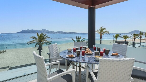 A round table with white wicker chairs overlooking a beach with clear blue water and distant mountains. - Ático Londres Derecha a Modern 2º floor Penthouse Beachfront in Puerto Pollensa (Puerto Pollensa)