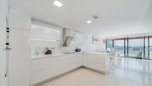 A modern kitchen with white cabinetry, a built-in oven, and a view of the sea through large windows. - Ático Londres Derecha a Modern 2º floor Penthouse Beachfront in Puerto Pollensa (Puerto Pollensa)