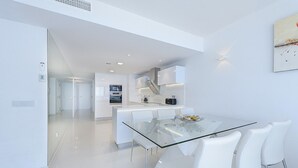 A modern kitchen with white cabinetry, a glass dining table, and white chairs. - Ático Londres Derecha a Modern 2º floor Penthouse Beachfront in Puerto Pollensa (Puerto Pollensa)