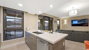 Une cuisine moderne dotée d’un grand îlot central, d’un coin repas avec un canapé gris et d’un téléviseur fixé au mur.
