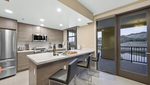 Une cuisine moderne dotée d’un îlot central, d’appareils électroménagers en acier inoxydable et offrant une vue sur un paysage montagneux grâce à de grandes portes coulissantes en verre.