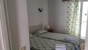 Un dormitorio con dos camas, una mesita de noche con lámpara y una ventana con cortinas estampadas.