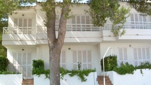 Un edificio de dos pisos con paredes exteriores blancas, un balcón en el piso superior y un árbol en la parte delantera.