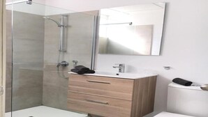 Un baño moderno con ducha de vidrio, tocador de madera con lavamanos y un inodoro.