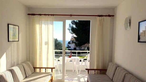 Una habitación con dos sofás a rayas, una mesa de madera y vistas a un balcón con mobiliario exterior.