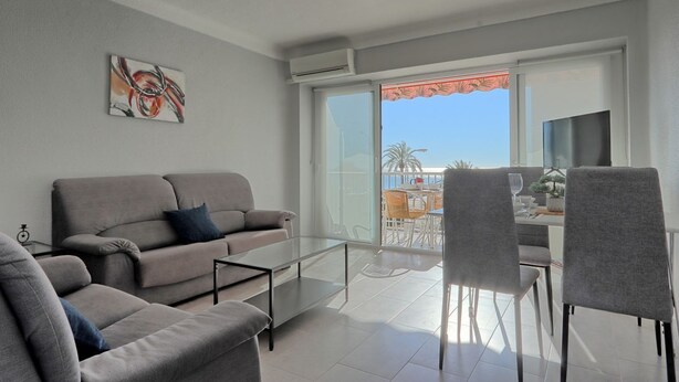 A modern living room with a grey sofa, a glass coffee table, and a balcony with a view of the sea. - 036 - Sierramar 001 - comfortHOLIDAYS (Santa Pola)