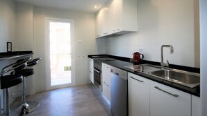A modern kitchen with white cabinets, a black countertop, stainless steel appliances, and a red kettle. - 036 - Sierramar 001 - comfortHOLIDAYS (Santa Pola)