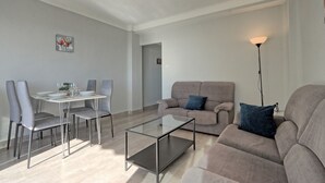 A modern living room with a glass coffee table, grey sofas, and a dining area with chairs and a table set for two. - 036 - Sierramar 001 - comfortHOLIDAYS (Santa Pola)