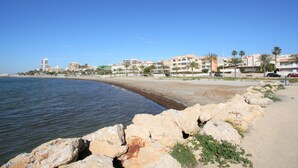 A coastal area with a rocky shoreline, a sandy beach, and buildings in the background. - 036 - Sierramar 001 - comfortHOLIDAYS (Santa Pola)