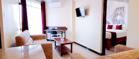 A hotel room with a dining area, a TV mounted on the wall, and a bed with a canopy.