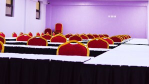 A conference room with rows of red chairs and black tables, purple walls, and a red chair with a gold frame in the back. - Divine Homes Resort (Kisumu)