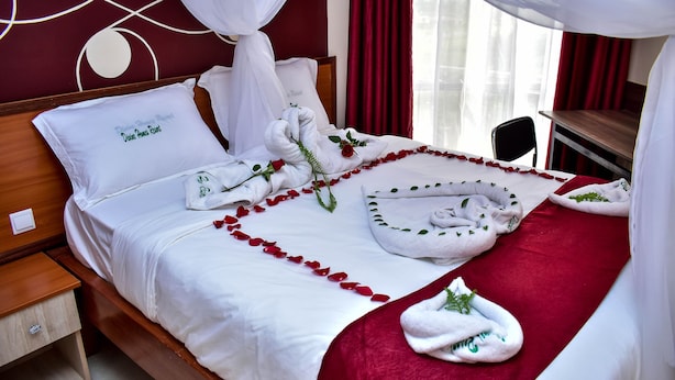 A neatly made bed with white linens, red rose petals, and towels arranged artistically. - Divine Homes Resort (Kisumu)