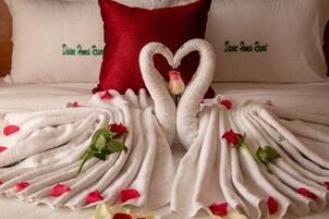 Una cama con toallas blancas dispuestas en forma de corazón, una rosa y pétalos de rosa esparcidos alrededor.
