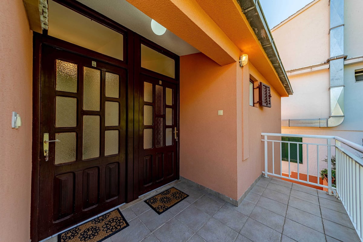 A building entrance with two large wooden doors, a small balcony with a white railing, and a tiled floor.