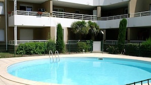 A swimming pool surrounded by a multi-story building with balconies, a gated entrance, and some greenery. - Lovely T2 with pool-near city and transport (CARCASSONNE)