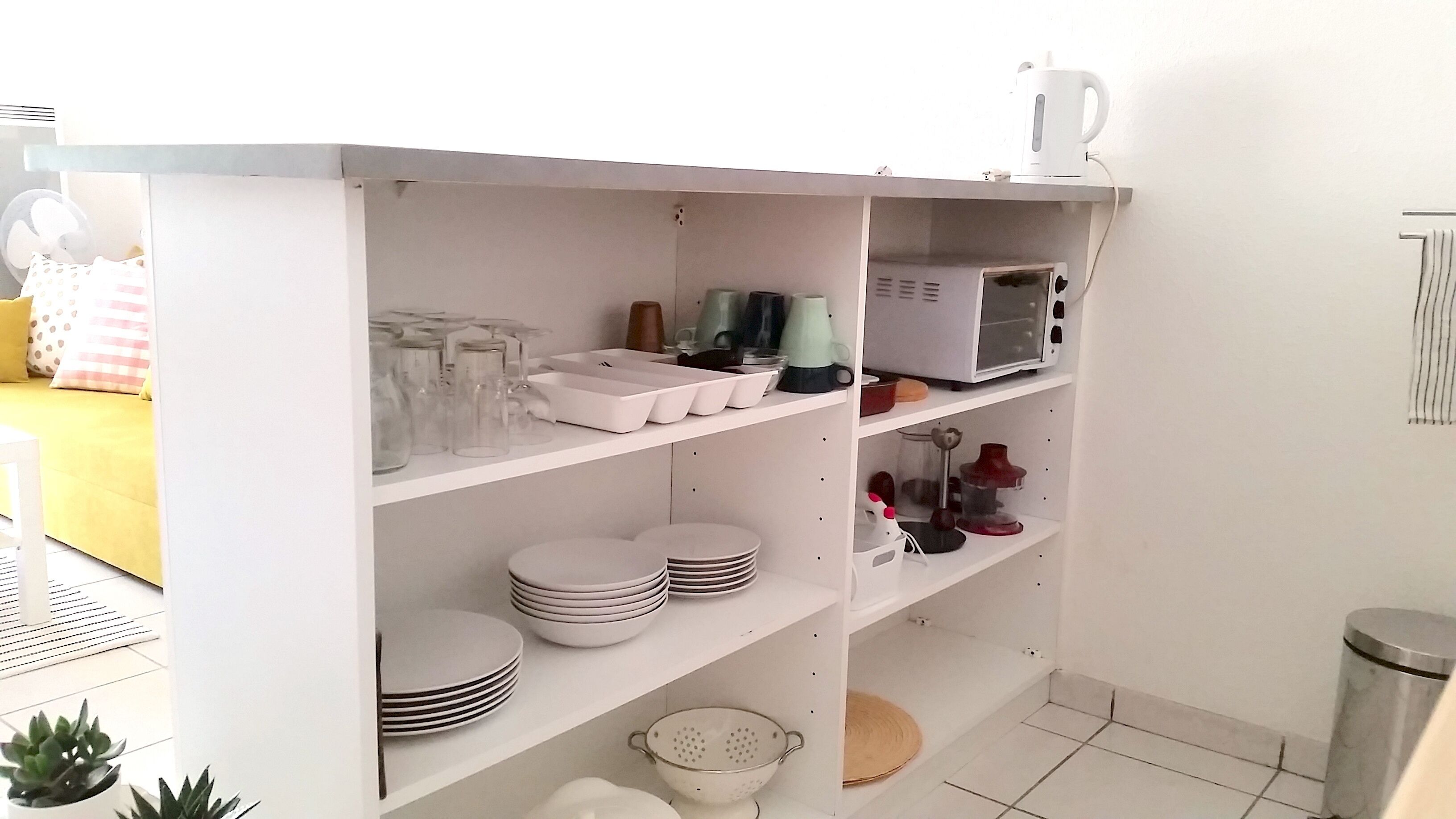 A white shelving unit with glassware, plates, and a microwave.
