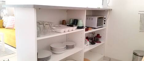 A white shelving unit with glassware, plates, and a microwave.