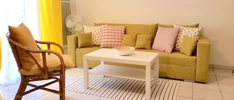 Una sala de estar con un sofá amarillo, una mesa de centro blanca y una silla de mimbre.