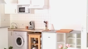 A modern kitchen with white cabinets, a microwave, and a washing machine. There is a dining table with a striped tablecloth and a vase with flowers. - Lovely T2 with pool-near city and transport (CARCASSONNE)