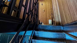 Una escalera de madera con barandales de metal que lleva a una puerta con un pequeño marco de fotos y un perchero.