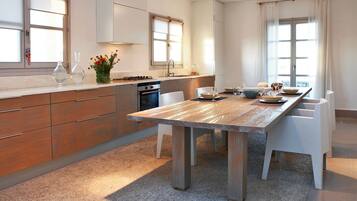 A modern kitchen with a wooden table, white chairs, and a large window.