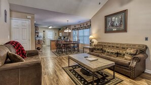 Un salon spacieux avec un canapé en cuir marron, une table basse en bois et un tapis à motifs.
