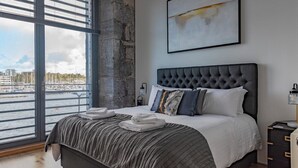 Une chambre moderne avec un grand lit, une vue sur un port de plaisance et un mur en pierre.