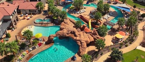 Un complexe hôtelier doté de plusieurs piscines, dont une grande piscine centrale et une plus petite agrémentée d’une formation rocheuse. On y trouve également des espaces de détente avec des parasols et des chaises longues.