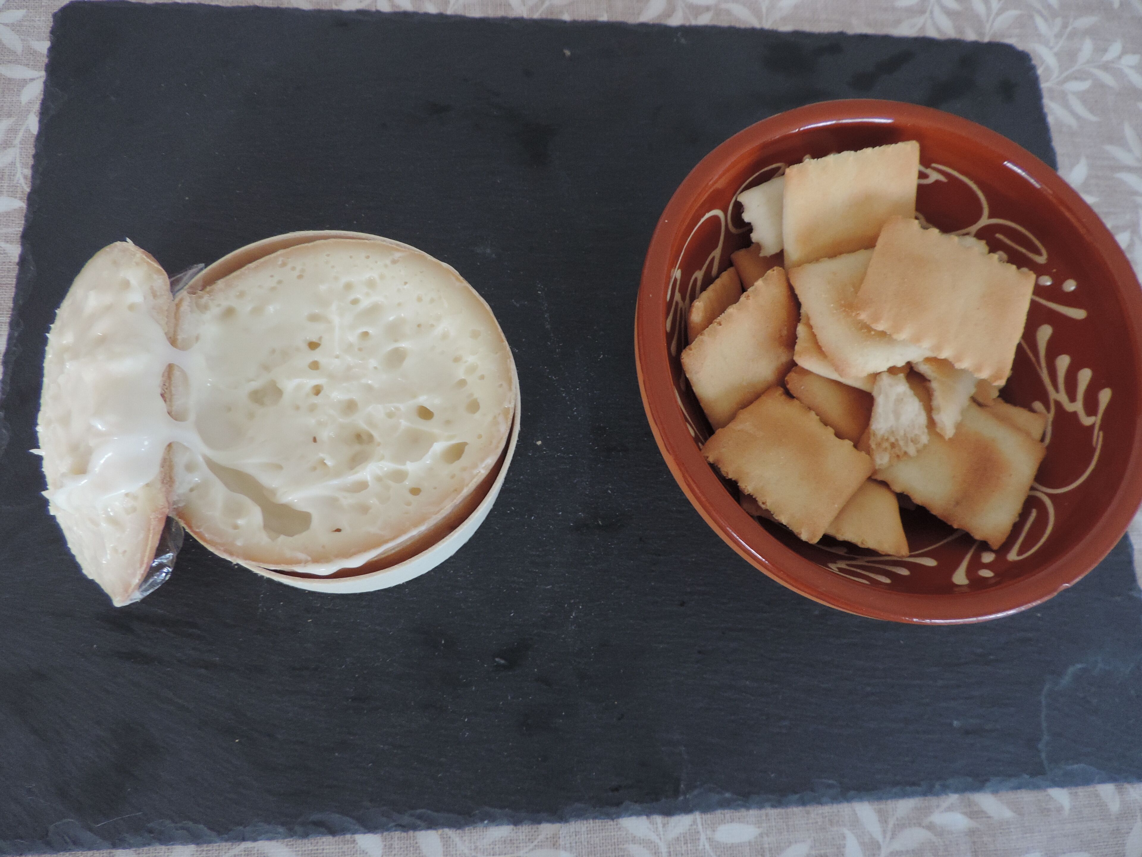 Una pizarra de piedra negra con un cuenco de galletas y un pastel de queso a medio comer.