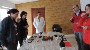 Un grupo de personas alrededor de una mesa con comida y vino, en una habitación con paneles de madera y una puerta.