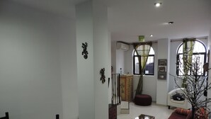 Una sala de estar con un sofá, una mesa de comedor con sillas, una planta decorativa y una ventana con cortinas.