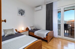 Ein Hotelzimmer mit zwei Einzelbetten, einem kleinen Nachttisch mit Lampe, einer Wand-Klimaanlage und einer Glastür zum Balkon.